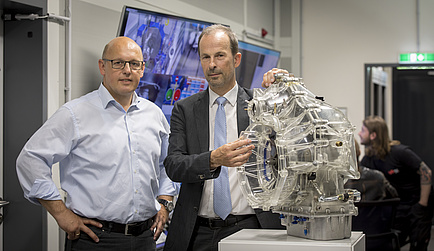 Three men talking surrounded by a notebook and a gearbox