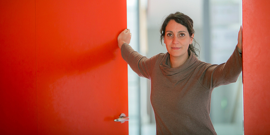 A dark-haired woman opening a red door.