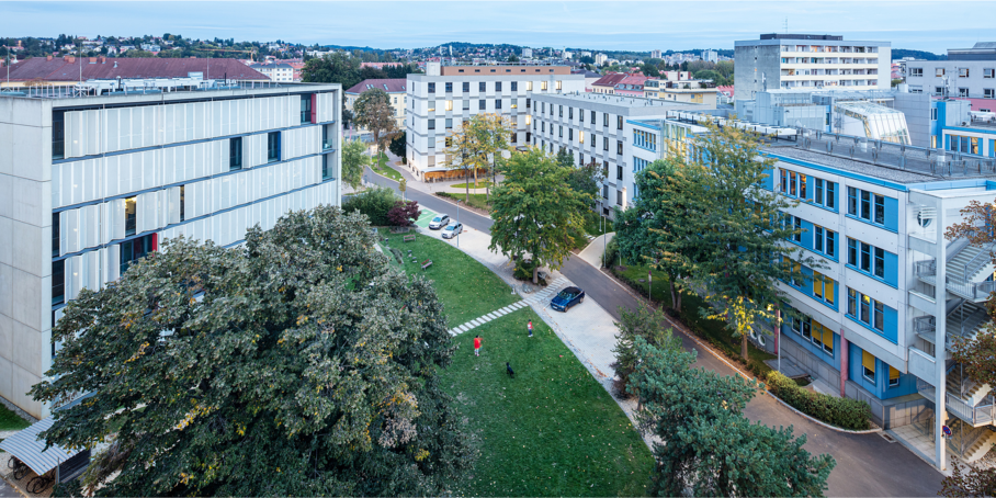 Mehrere Gebäude vom Campus Neue Technik der TU Graz, dazwischen ein Park mit Bäumen und Wiesen.