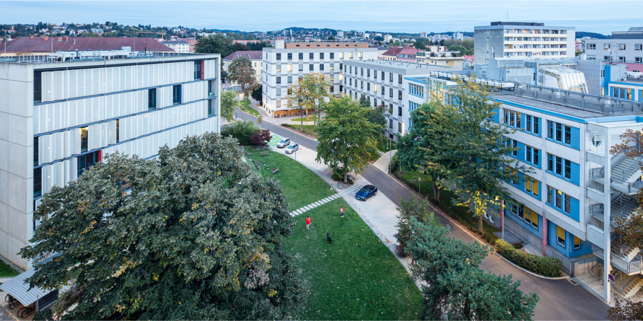 Several buildings from Graz University of Technology - New Campus, in between a park with trees and meadows.