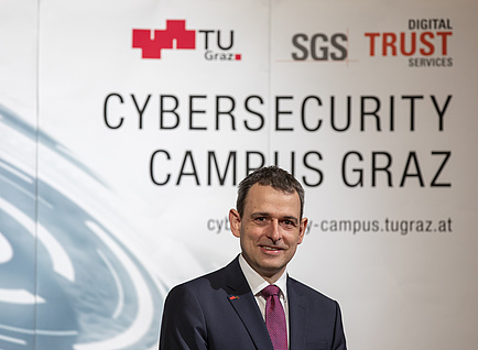 A man in a suit stands in front of the expo wall of the Cybersecurity Campus Graz