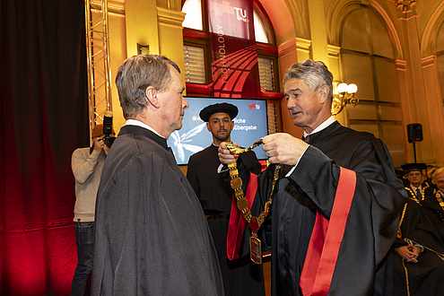 A man hands another man a gold chain.