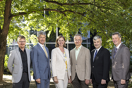 Eine Gruppe von sechs Menschen steht in einem Park und schaut in die Kamera.