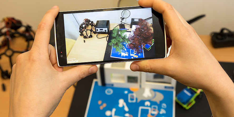 A Smartphone held by two hands. On the screen you can see the visualization of a test setup at Know-Center.