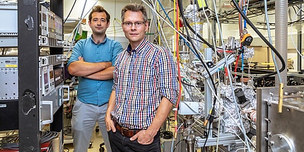 Two researchers in a physics lab, amidst cables and equipment