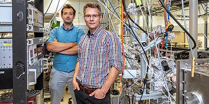 Zwei TU Graz Forscher in einem Physiklabor inmitten von Kabeln und Geräten