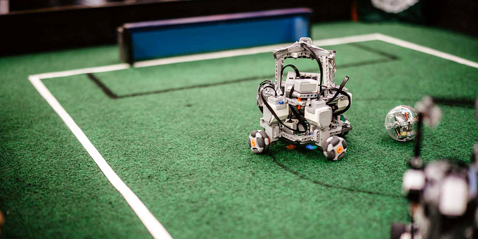 Ein Roboter steht auf einem Miniatur-Fußballfeld.