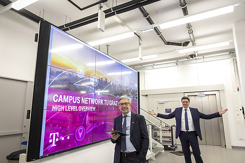 Two TU Graz researchers stand next to a monitor wall