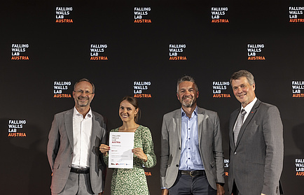 Four people smile into the camera, the second person from the left holds a document that says she has won second place