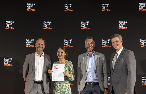 Four people smile into the camera, the second person from the left holds a document that says she has won second place