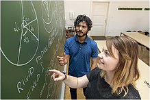 A woman and a man in front of a blackboard inscribed with chalk.