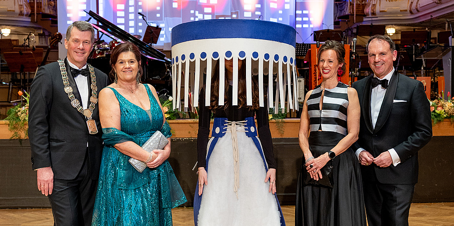 5 Personen stehen festlich gekleidet in einem Ballsaal. Die Person in der Mitte trägt eine Verkleidung auf dem Kopf – es sieht aus wie ein Lampenschirm. 