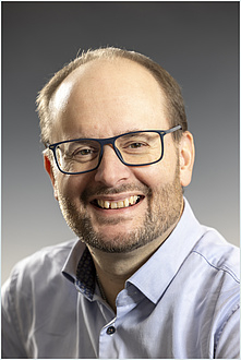 A man with glasses smiles into the camera