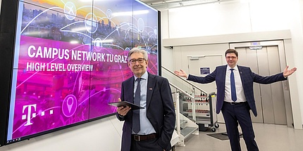 Zwei TU Graz-Forscher vor einem überdimensional großen Bildschirm