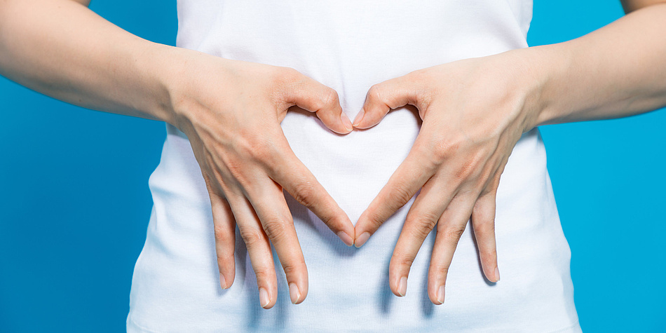 Ein aus zwei Händen geformtes Herz vor dem Bauch einer Person