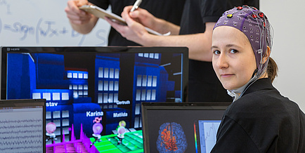 Woman with electrode cap in front of computer screens with games