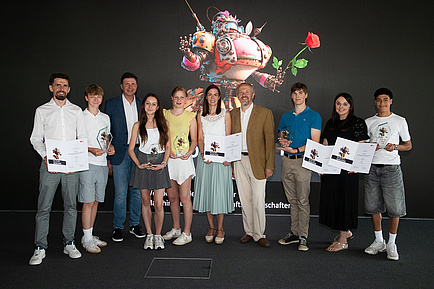 Ten people stand next to each other on a stage and smile into the camera.