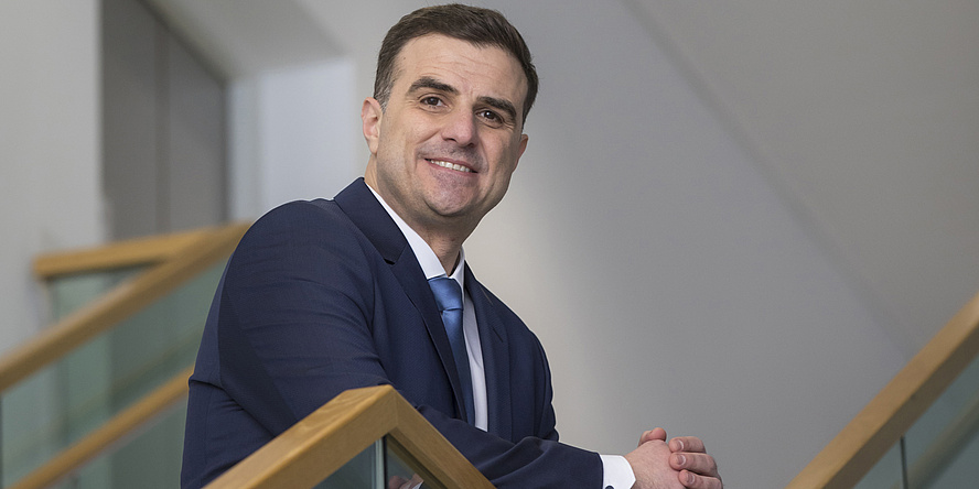 A portrait of Sergio Amancio. He wears brown, short hair, a blue suit, white shirt and blue tie. 