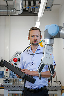 [Translate to Englisch:] TU Graz researcher operates collaborative robot arm