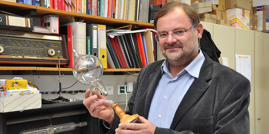 Gernot Pottlacher steht in seinem Büro und hält eine Glasröhre in der Hand.