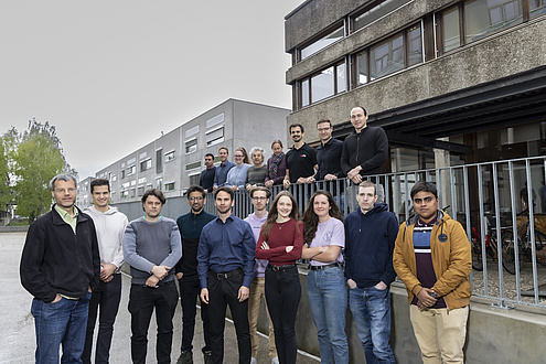 A group of people is standing in front of a building and look into the camera.