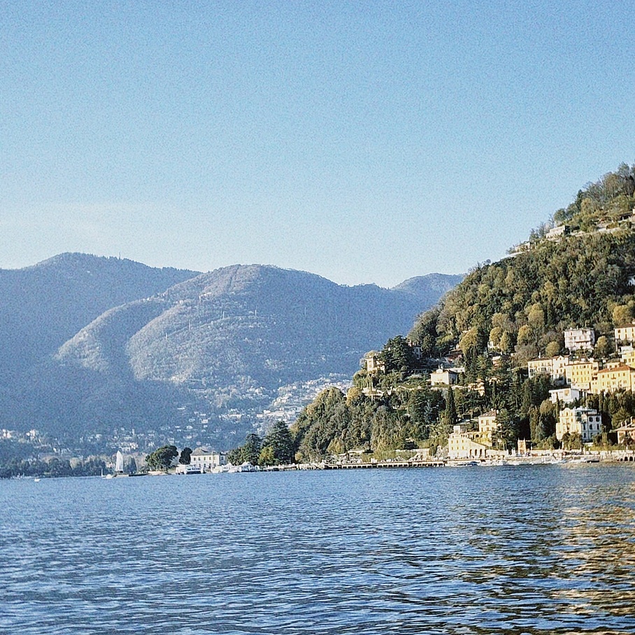 Blick über einen blau-grünen See zu sanften begrünten Hügeln, die den See umrahmen.