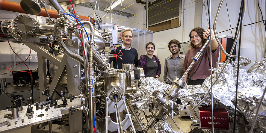 Vier Personen stehen in einem Physiklabor