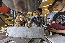 Drei Studierende platziern ein Betonbauteil in ein Testgerät.