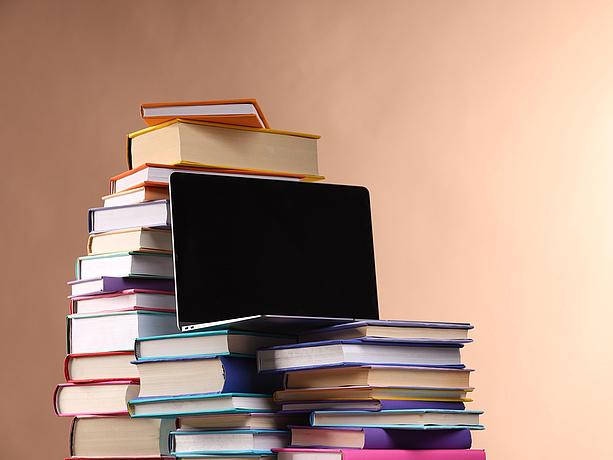 Stack of books and laptop, brown background.