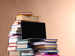 Stack of books and laptop, brown background.