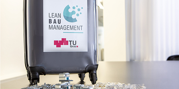 On a suitcase on a table is written: Lean Baumanagement. TU Graz