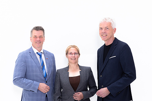 Drei Personen stehen beieinander und lächeln in die Kamera.