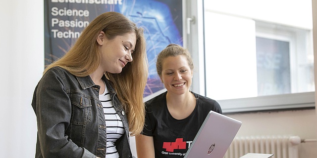 Zwei Studierende sitzen vor einem Laptop.