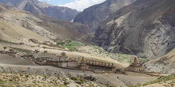 Several temple complexes stand on a plateau, with high mountain ranges in the background.