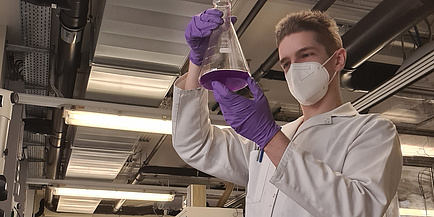 Junger Mann mit weißem Kittel und Maske im Labor
