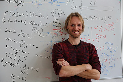 A man stands in front of a whiteboard on which formulas are written. 