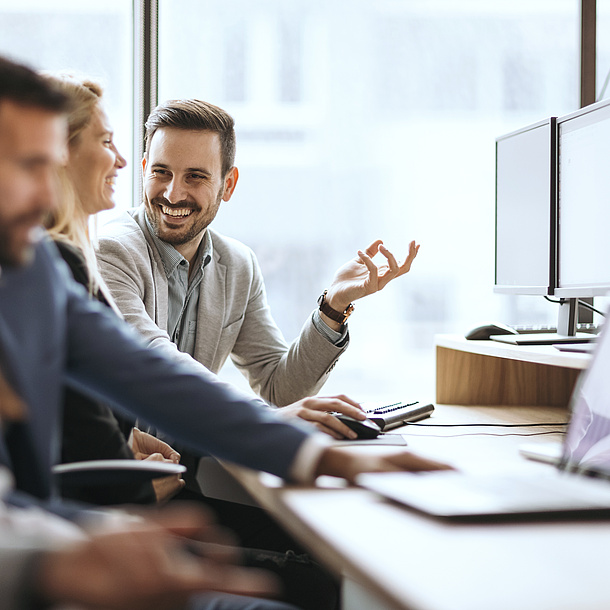 People are sitting at a desk and talk to each other.