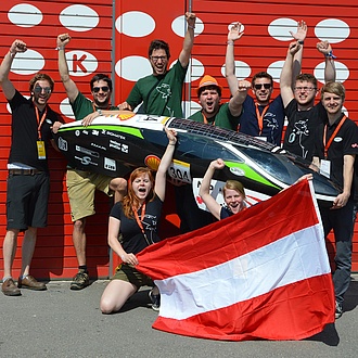 Jubelnde Studierende mit einem Leichtbaufahrzeug und Österreich-Fahne