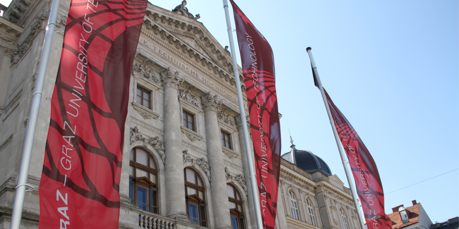 TU Graz Fahnen und im Hintergrund das Gebäude Alte Technik der TU Graz.