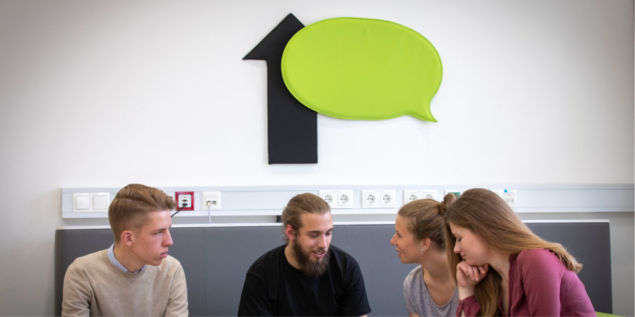 Two male and two female students sit together at the table and discuss.