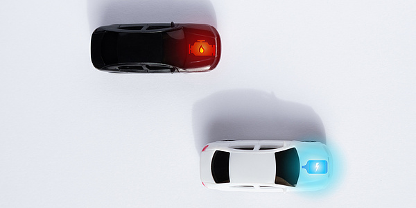 Graphic of two cars from a bird's eye view on a white surface. At the bottom right is a white car with an electric symbol on the bonnet. At the top left is a black car with the symbol for an internal combustion engine on the bonnet.