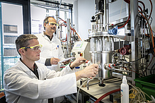 Two men with protective goggles and laboratory coats are working on a larger laboratory setup.