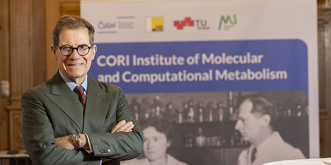 Ein Mann in einem Anzug lächelt in die Kamera. Er hat die Arme vor seiner Brust verschränkt.