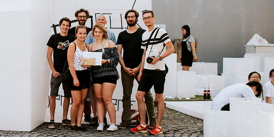 Fünf Studierende und zwei Betreuer der TU Graz stehen im Freien vor dem weißen "P-Cubed: ply-propylene"-Pavillon.