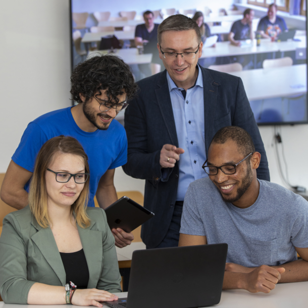 Teacher shows three students something on a laptop.