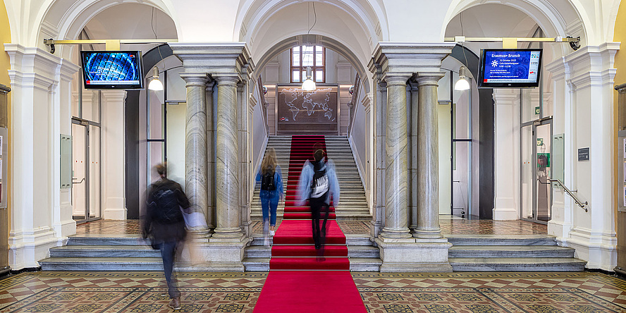 Stiegenaufgang mit rotem Teppich in der Eingangshalle eines historischen Universitätsgebäudes