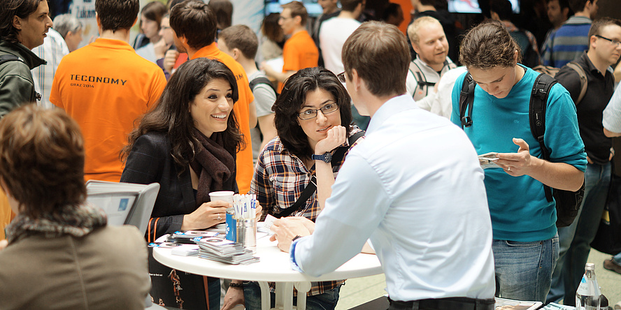 Two young women talk to an exhibitor at the TECONOMY careers fair at TU Graz.