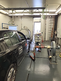 Photograph of a car on a test bench inside a small hall.