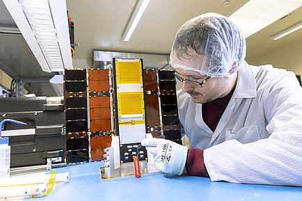 Man in lab coat and hair net works on a cube with folded-out side panels.