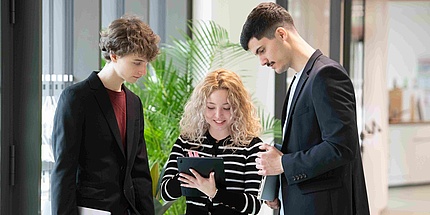 Three students look at a tablet computer while chatting.